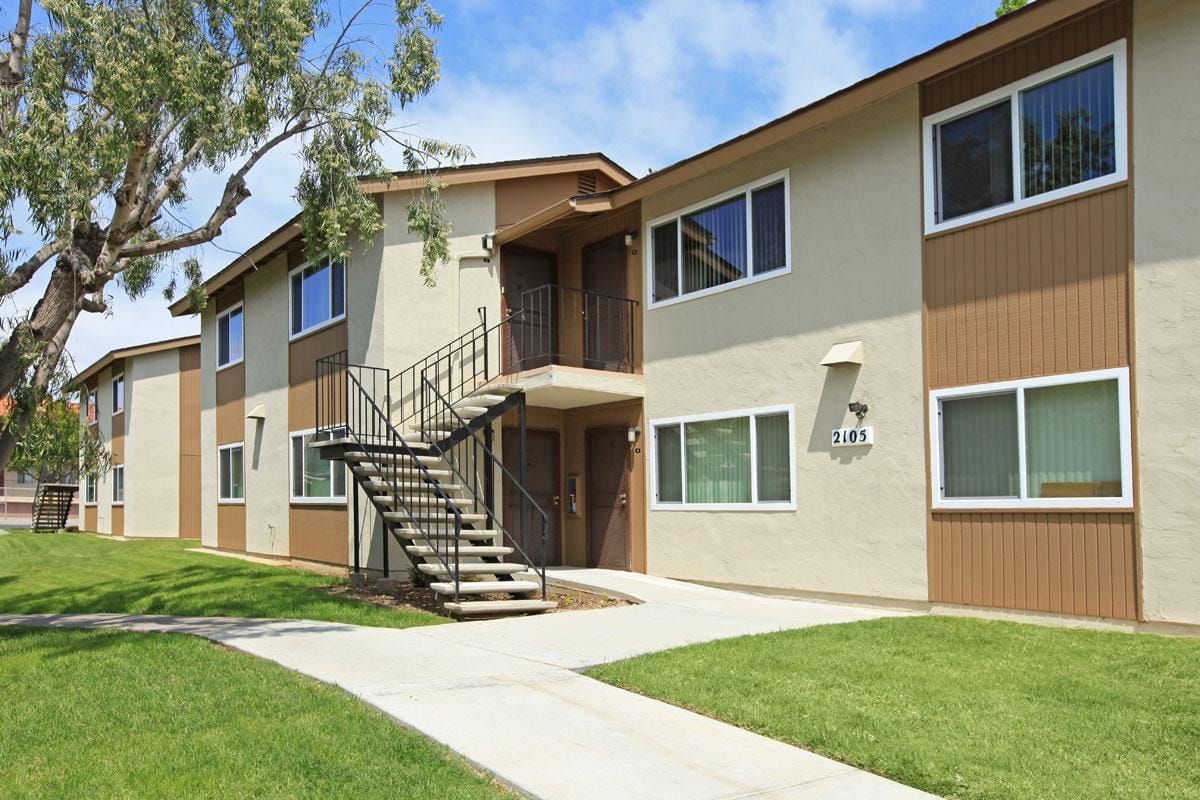 Exterior of a two story apartment building with green grass outside and a sidewalk.