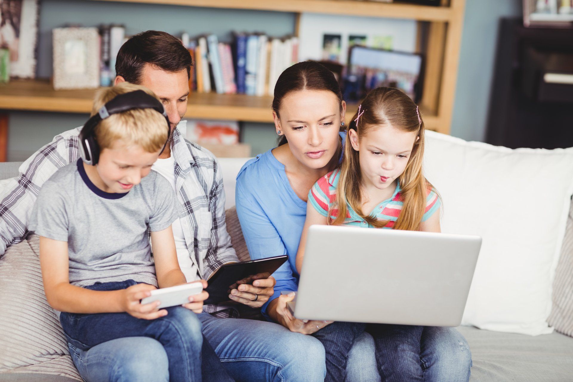 A family is sitting on a couch using a laptop and a tablet.