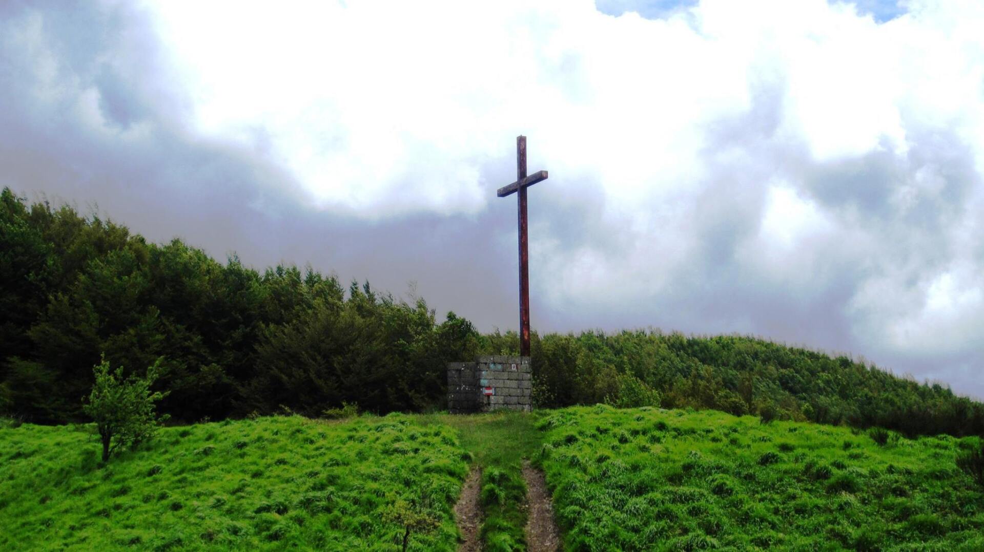 Una grande croce è posta in cima a una collina erbosa.