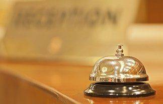 Il campanello di un hotel è appoggiato su un bancone di legno.