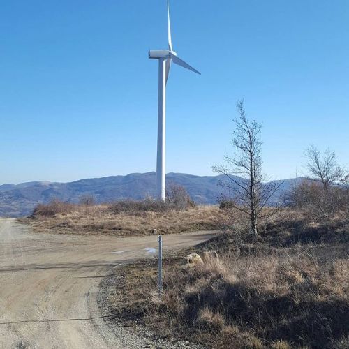 Una turbina eolica in cima a una strada sterrata con montagne sullo sfondo