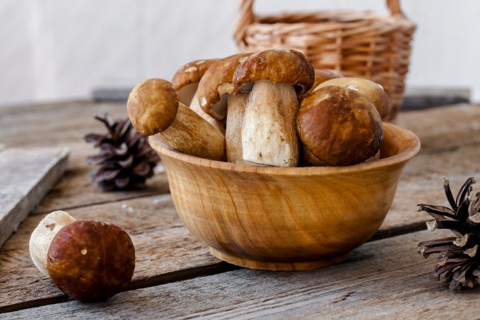 Una ciotola di legno piena di funghi su un tavolo di legno.