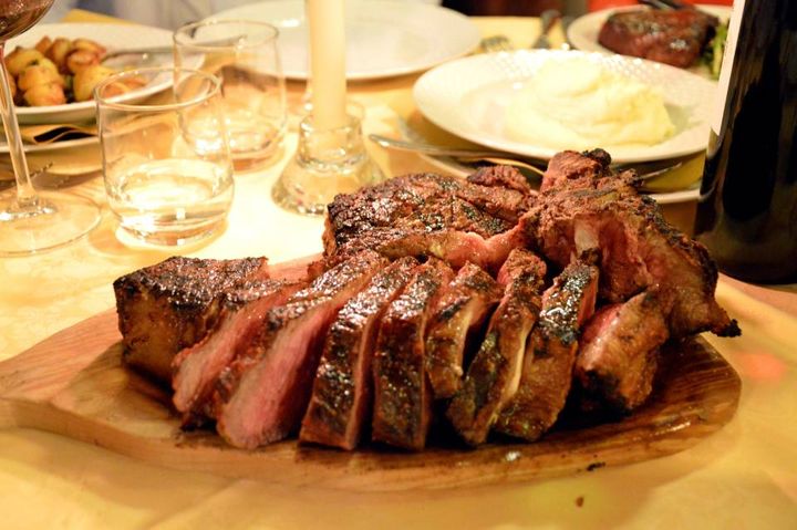 Un grosso pezzo di carne è appoggiato su un tagliere di legno su un tavolo.