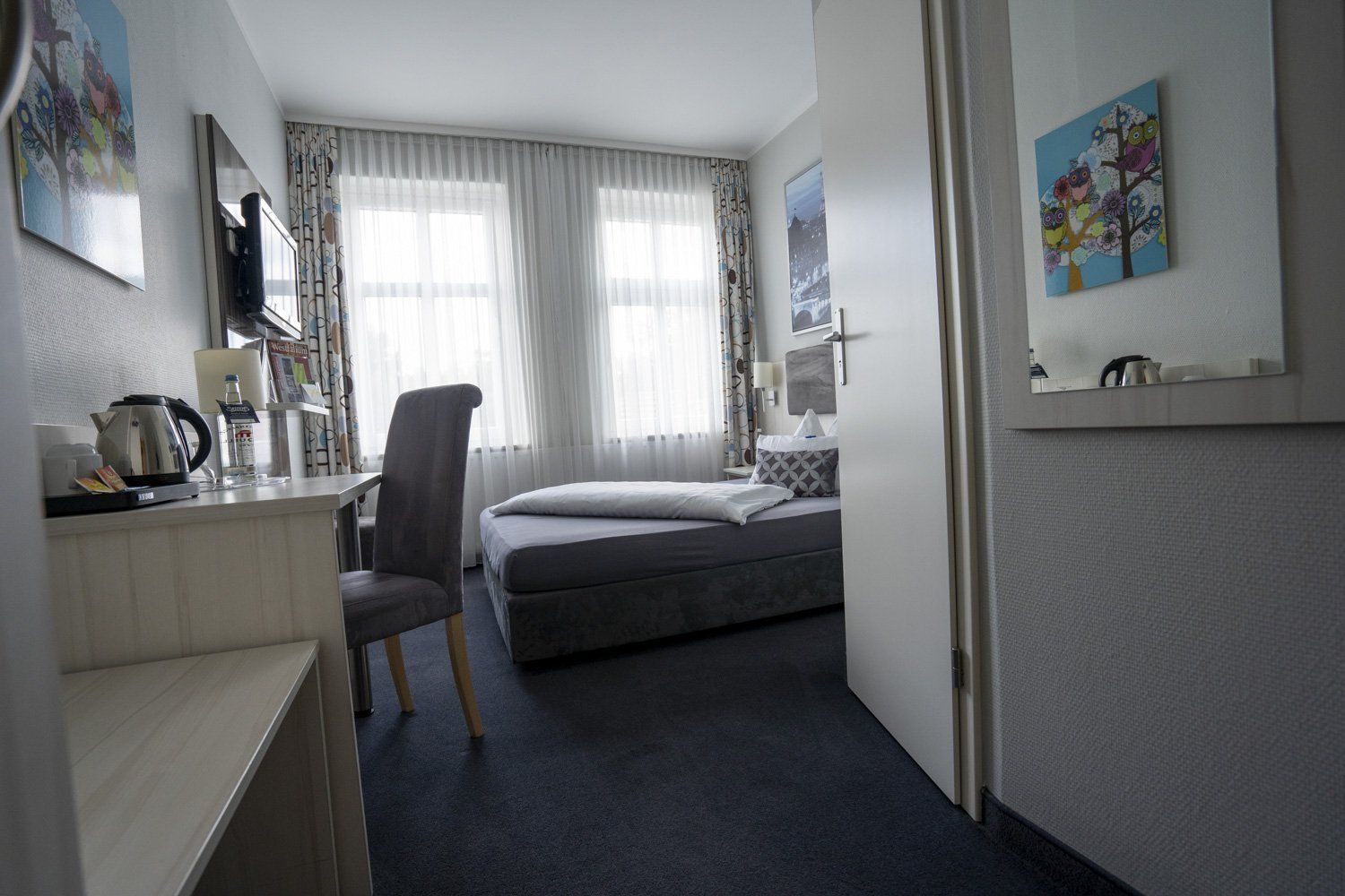 Ein Hotelzimmer mit Einzelbett, Schreibtisch, Stuhl und Spiegel.