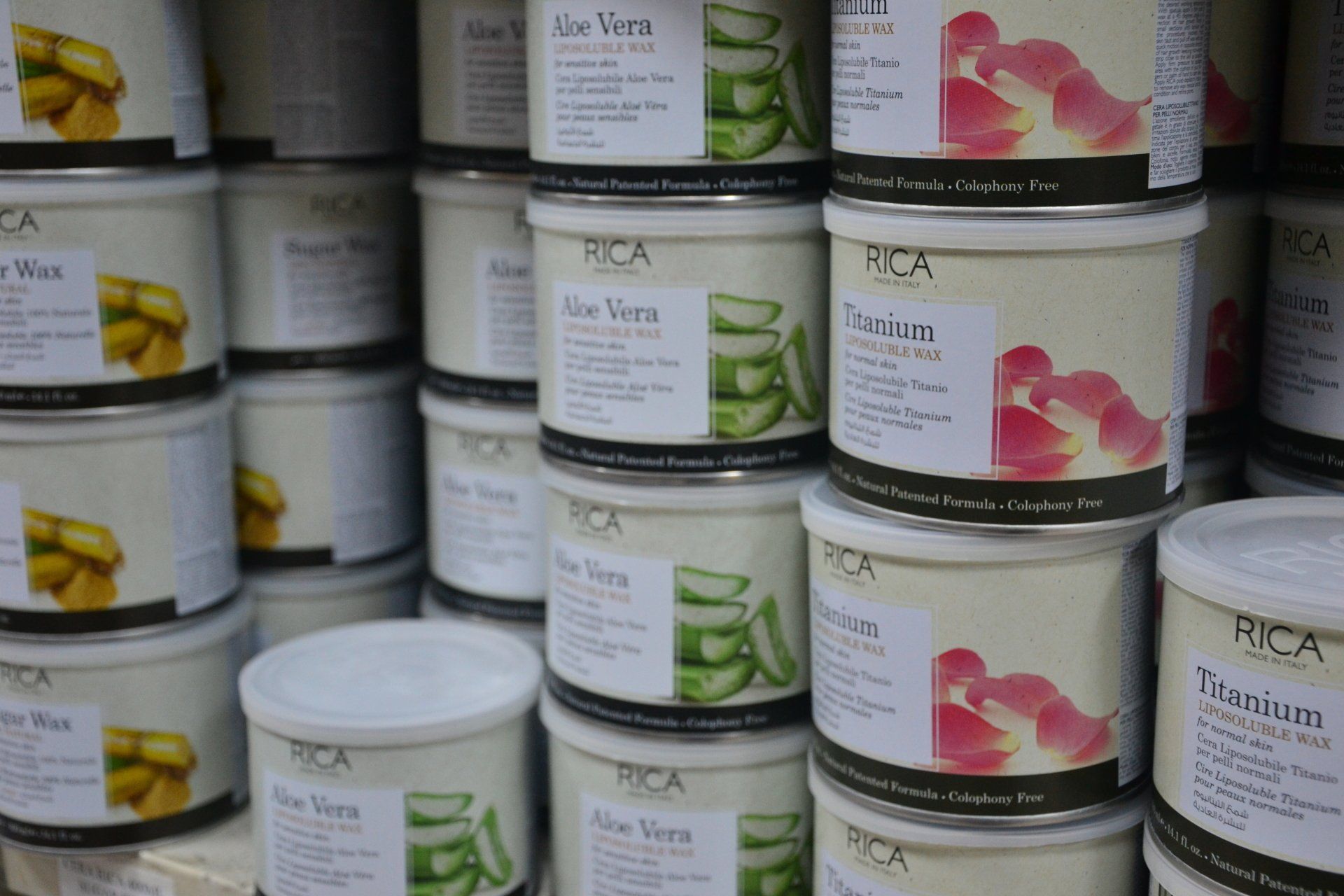 Pile di contenitori di cera RICA, etichettati con motivi di Aloe Vera e petali di rosa.