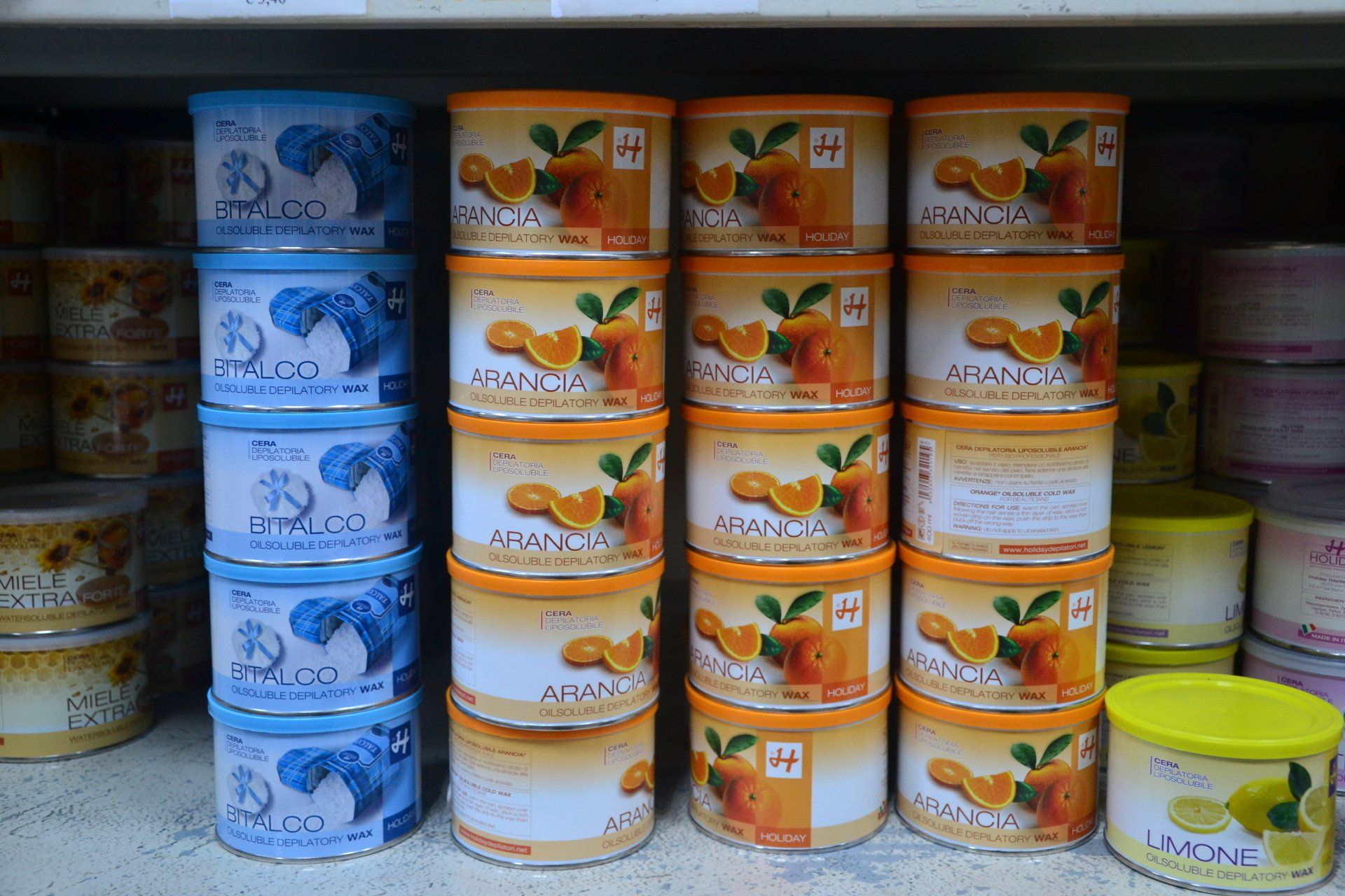 Prodotti in scatola su uno scaffale: pile di lattine con etichette blu, arancioni e gialle.
