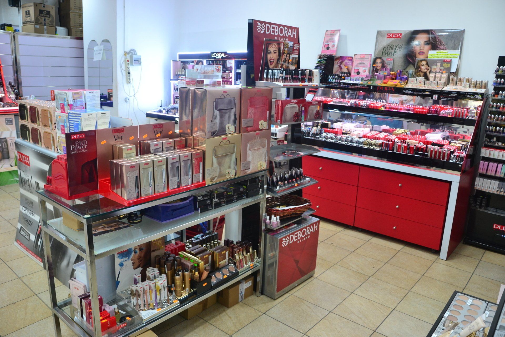 Interno di un negozio di cosmetici con scaffali espositivi pieni di prodotti per il trucco. Dettagli rossi e bianchi.