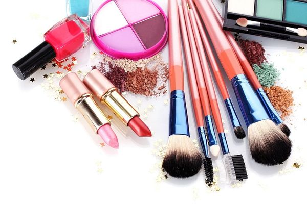 Prodotti per il trucco: rossetti, pennelli, ombretti, smalti e polveri sparse, su una superficie bianca.
