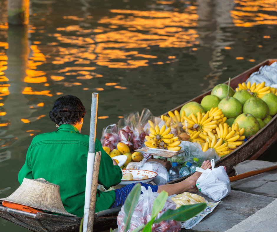 Eine Frau in einem grünen Hemd sitzt in einem Boot und verkauft Bananen und Äpfel.