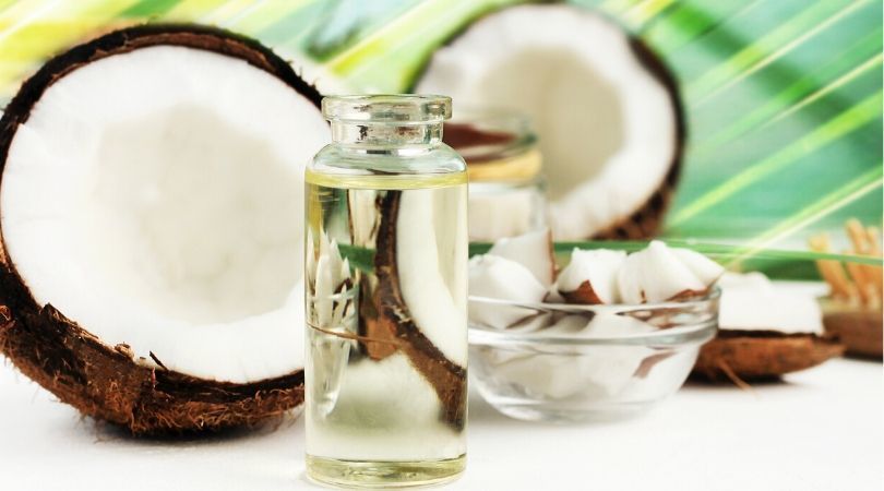 Eine Flasche Kokosnussöl steht neben einer Schale mit Kokosnüssen.