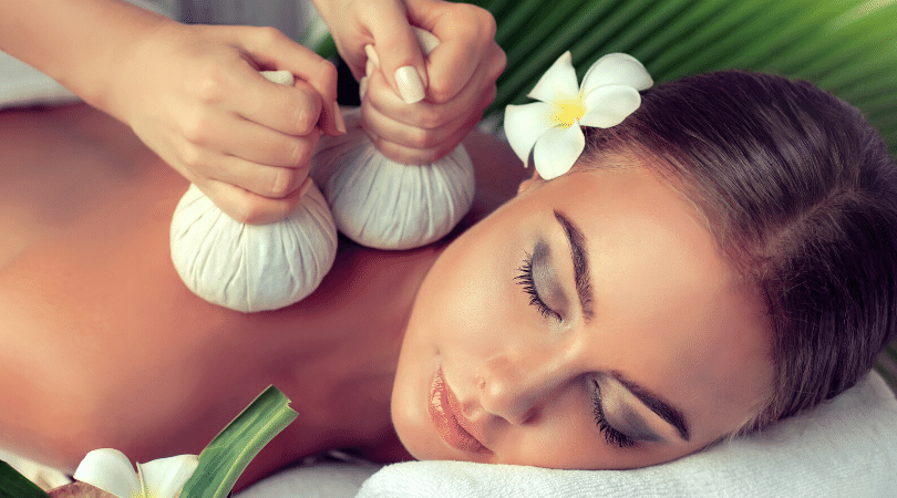 Eine Frau mit einer Blume im Haar bekommt in einem Spa eine Massage.