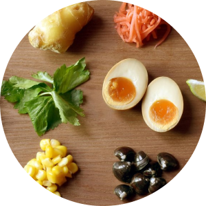 Ingredientes para um prato, incluindo ovos, milho, gengibre, coentro e azeitonas pretas, dispostos sobre madeira.