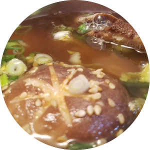 Close-up de cogumelo shiitake e carne bovina em um caldo escuro com cebolinha e sementes de gergelim.