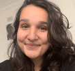 Mulher com cabelo escuro e cacheado sorri para a câmera.