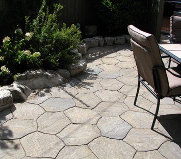 A patio with a table and chairs and a bush in the background