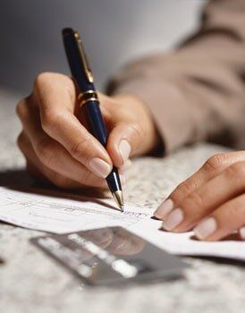 A hand holding a pen writing on a document; credit card visible in the foreground.