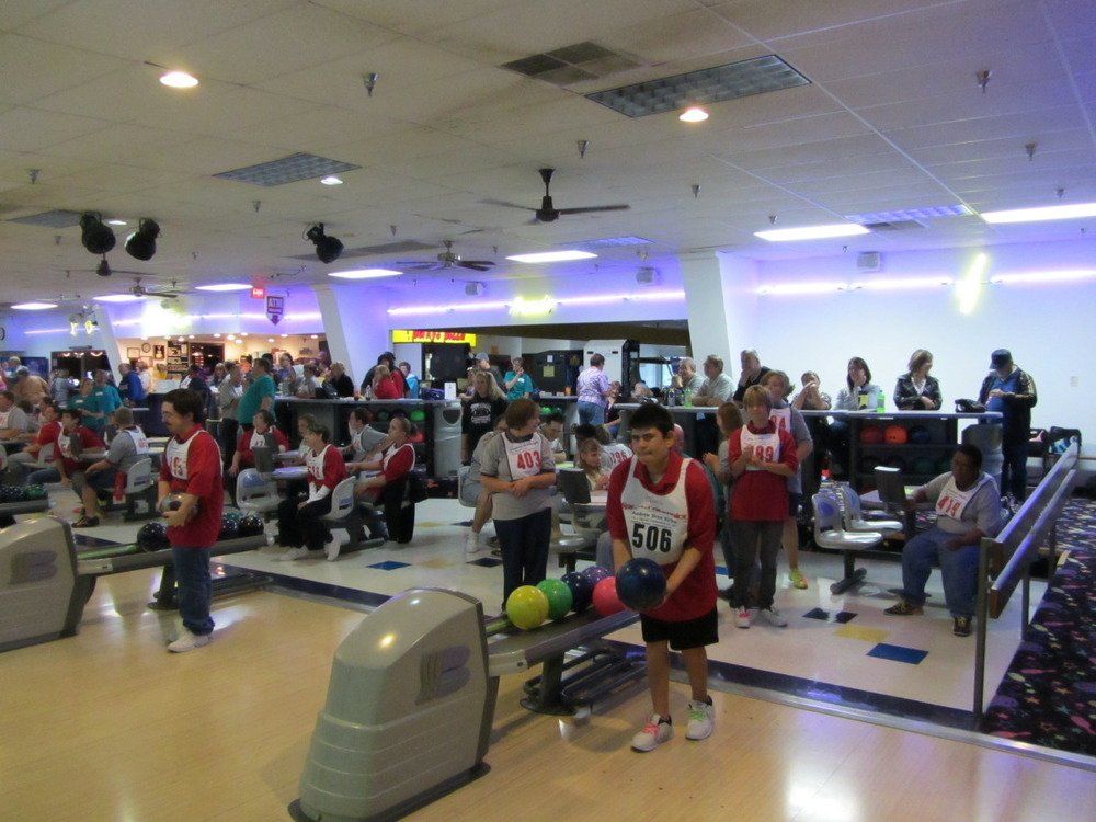A group of people are bowling in a bowling alley and one of them is wearing a shirt that says epb