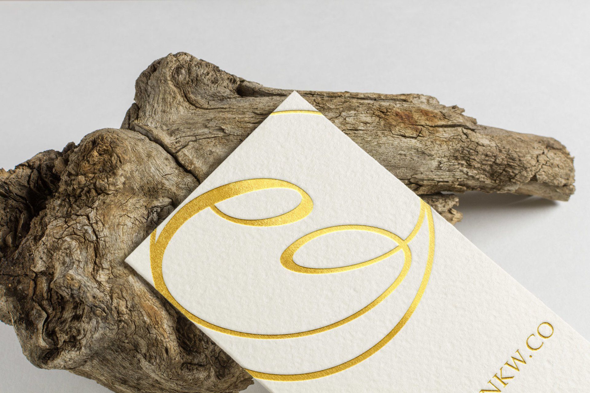 Gold-foil logo on a white business card, resting on a weathered piece of wood.