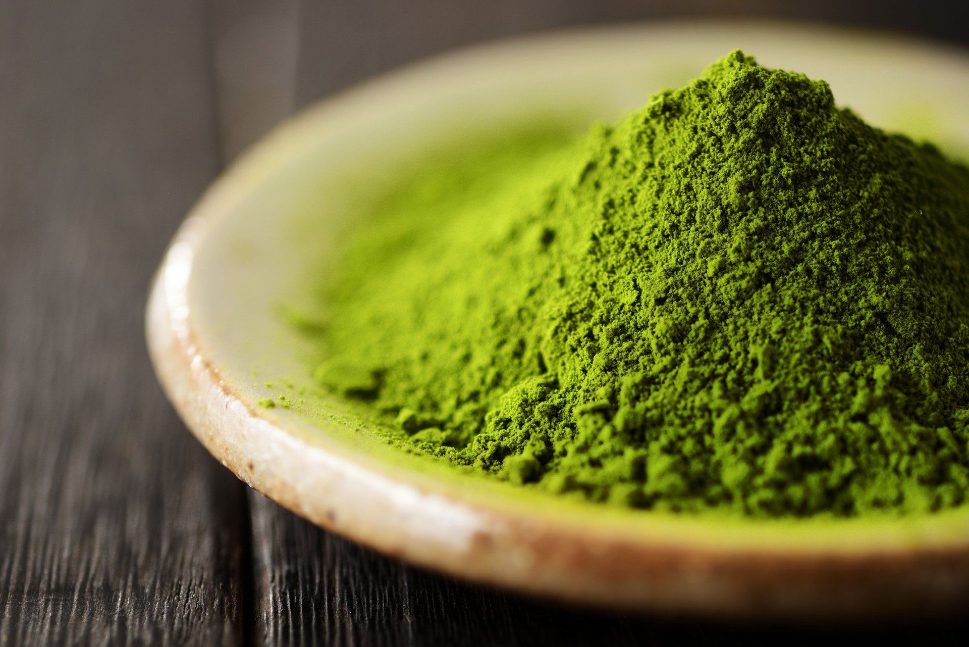 Green matcha powder in a small, off-white bowl on a wooden surface.