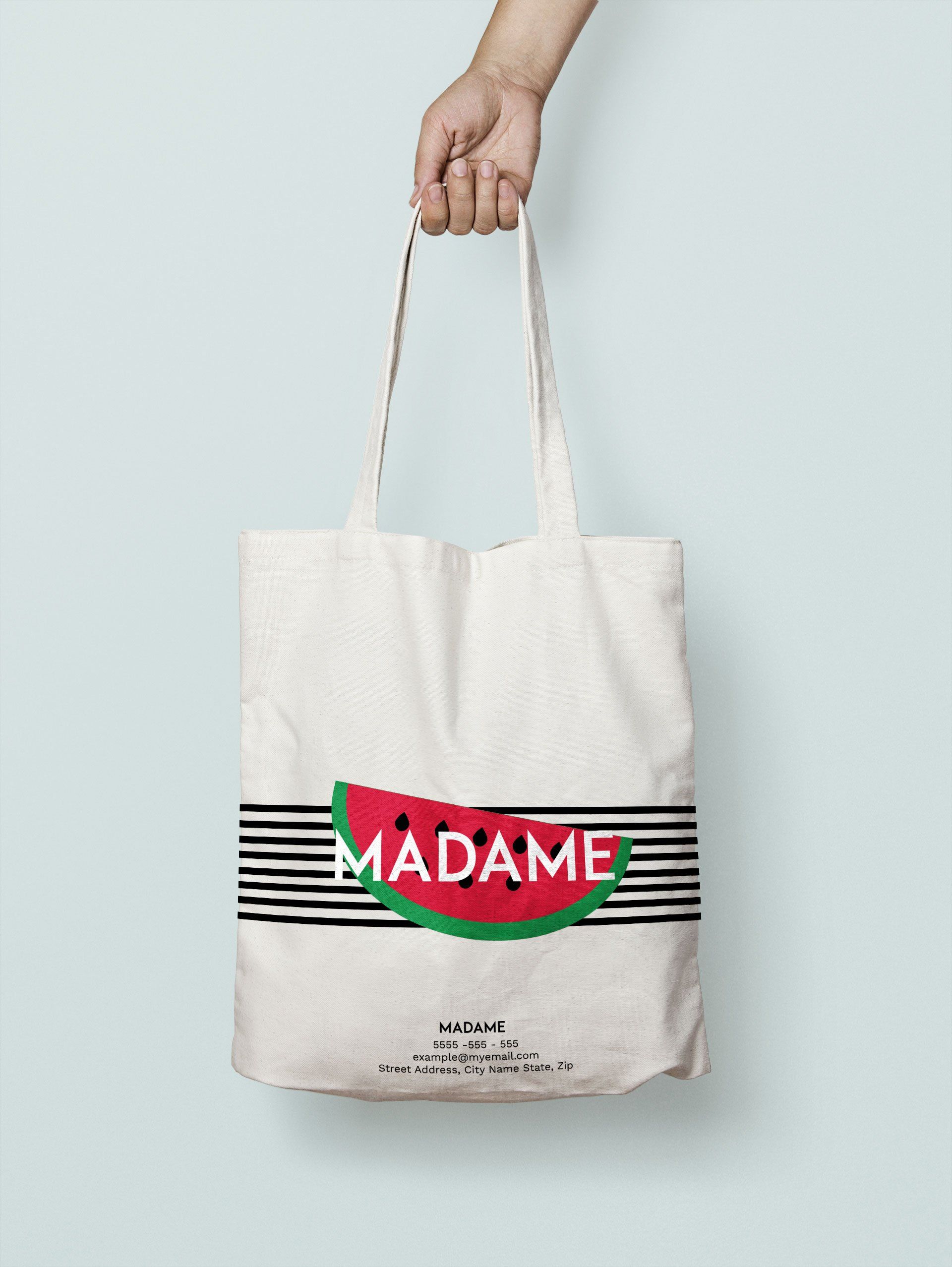 Hand holding a beige tote bag with a watermelon and 