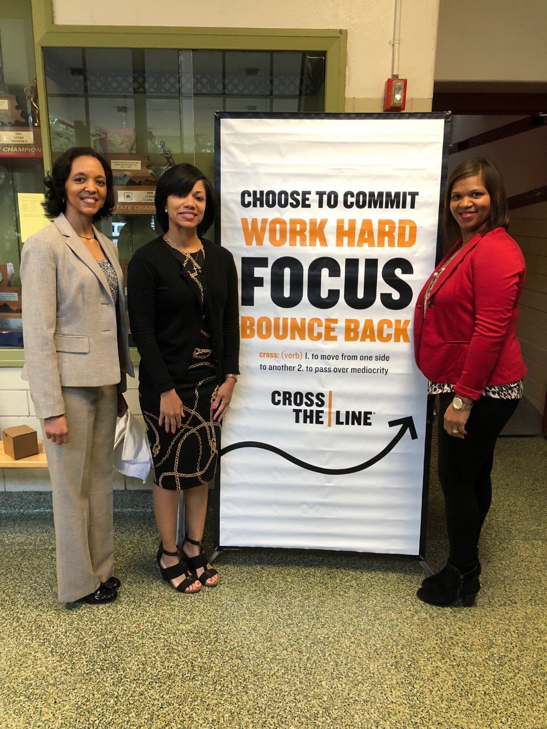 Three women are standing in front of a sign that says `` choose to commit work hard focus bounce back ''.
