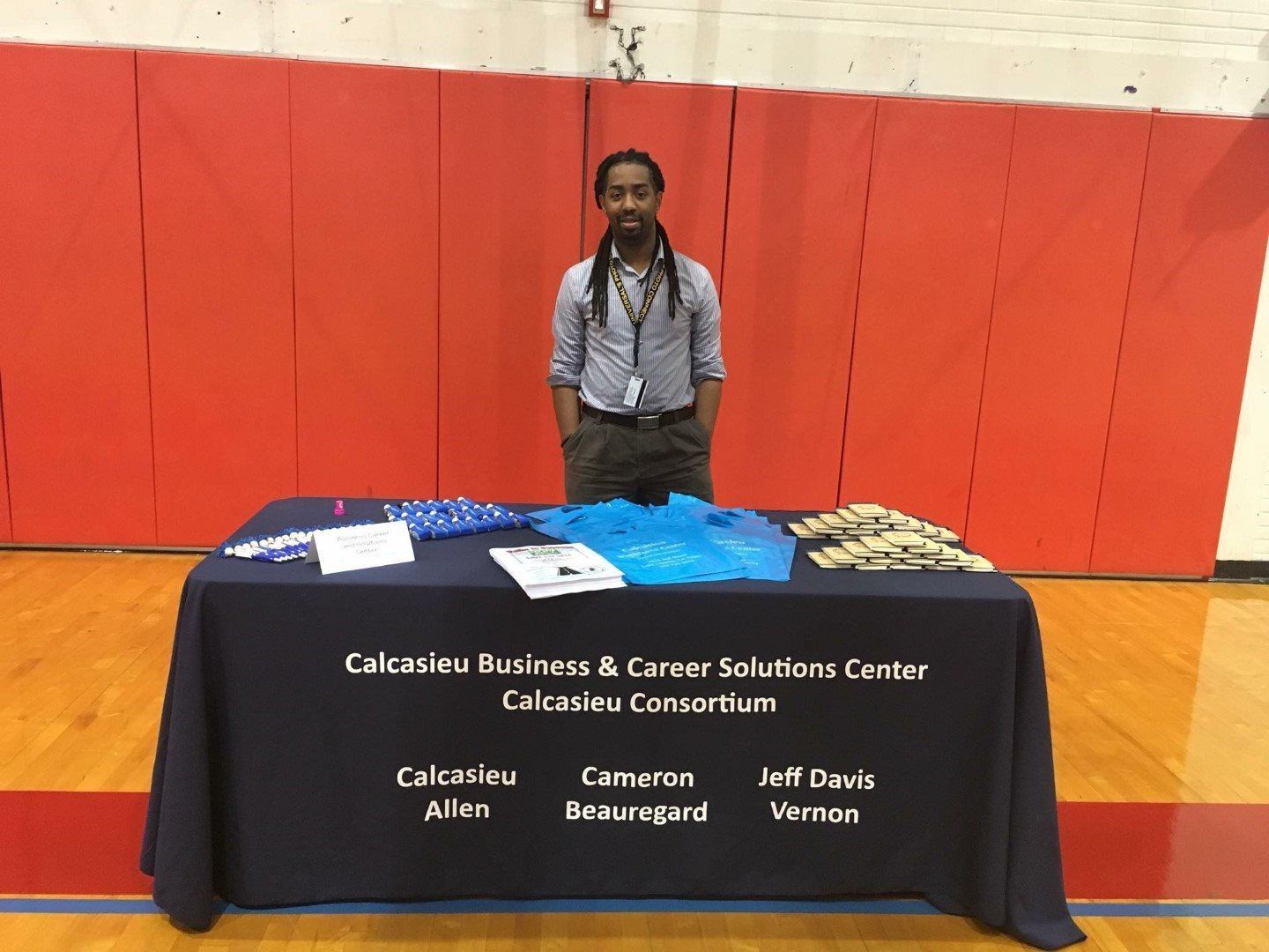 A man is standing in front of a table with a blue table cloth that says ' calcasieu business & career solutions center '
