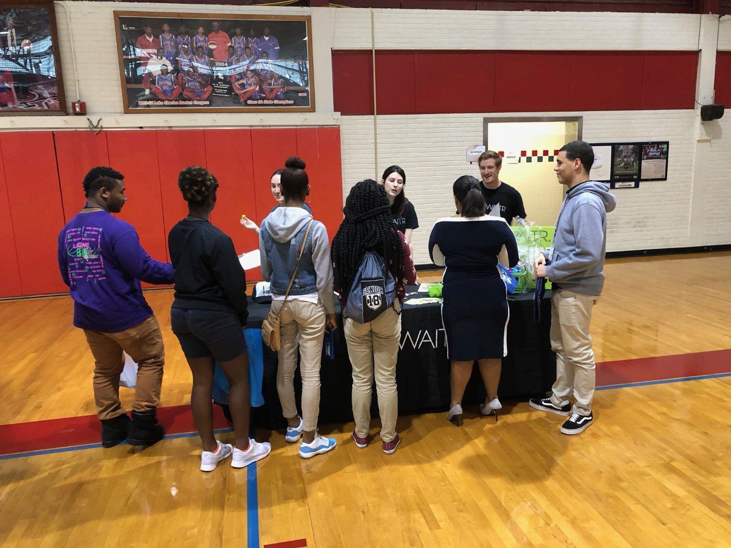 A group of people are standing around a table in a gym.