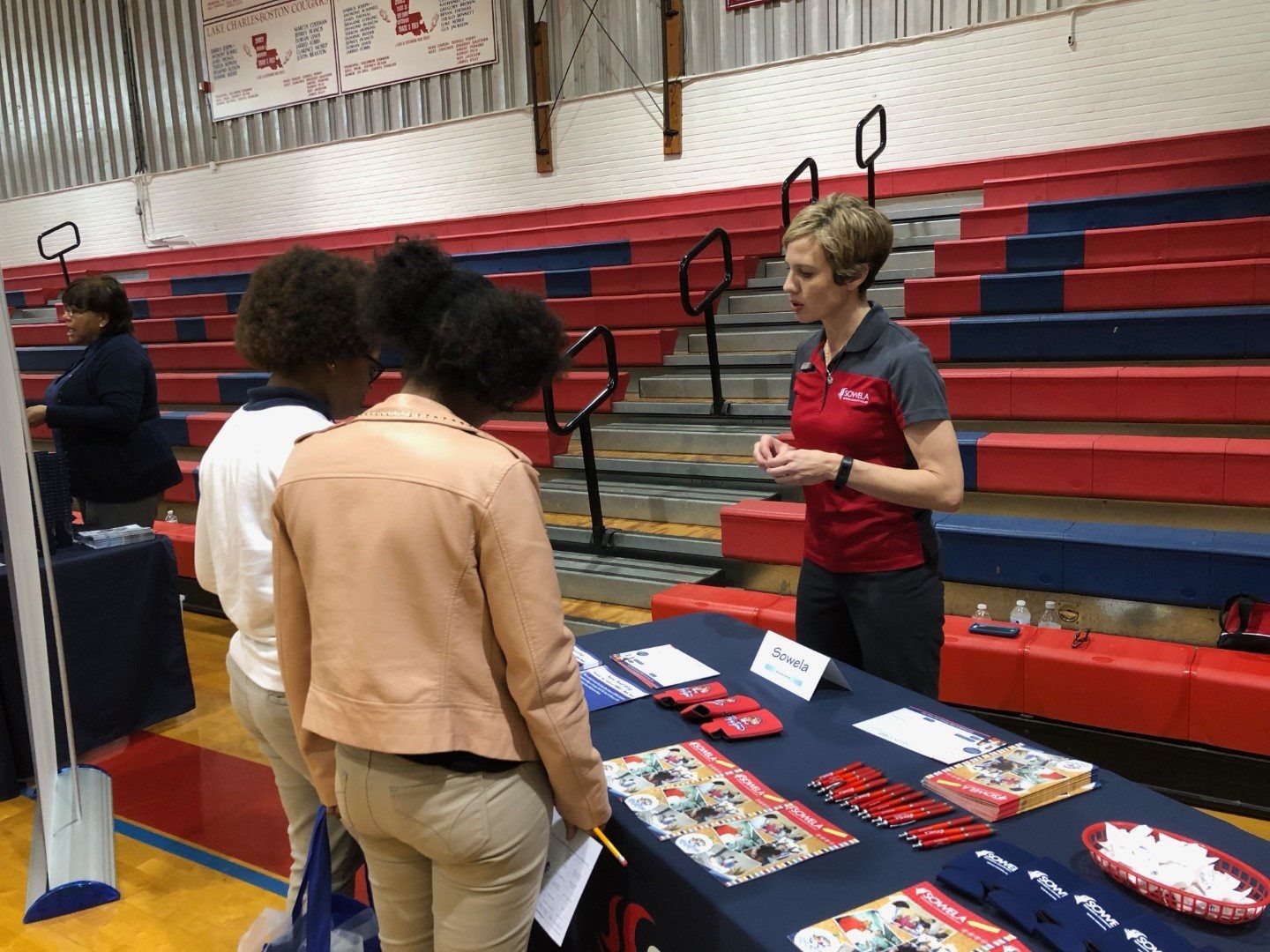 A woman is talking to a group of people at a table in a gym.