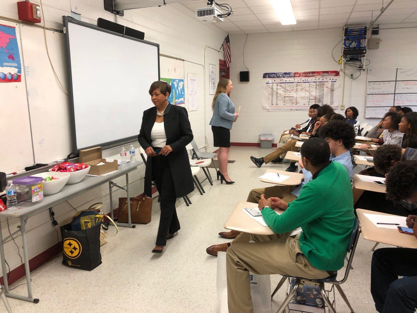 A woman is standing in front of a group of people in a classroom.