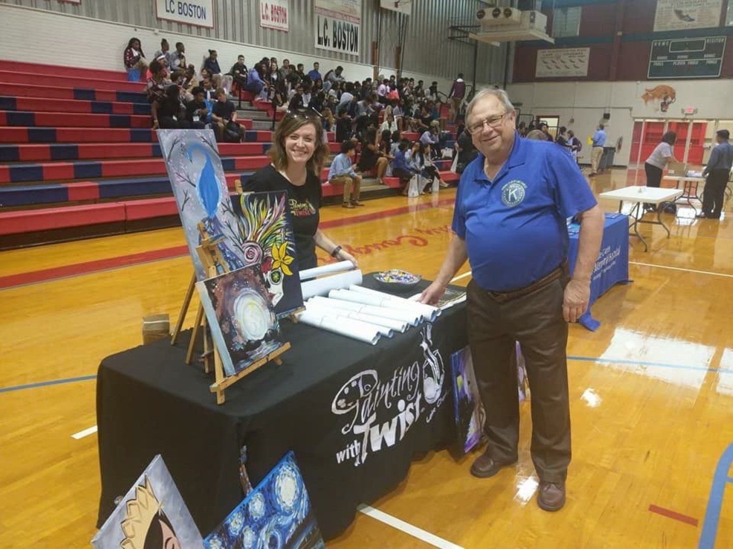 A man and a woman are standing next to a table in a basketball court.