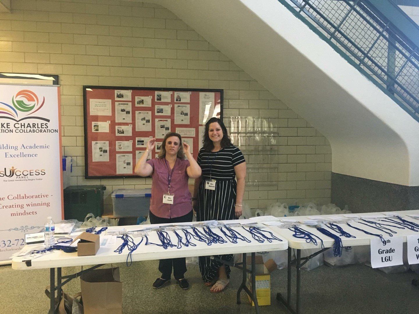 Two women are standing in front of a table with lanyards on it.