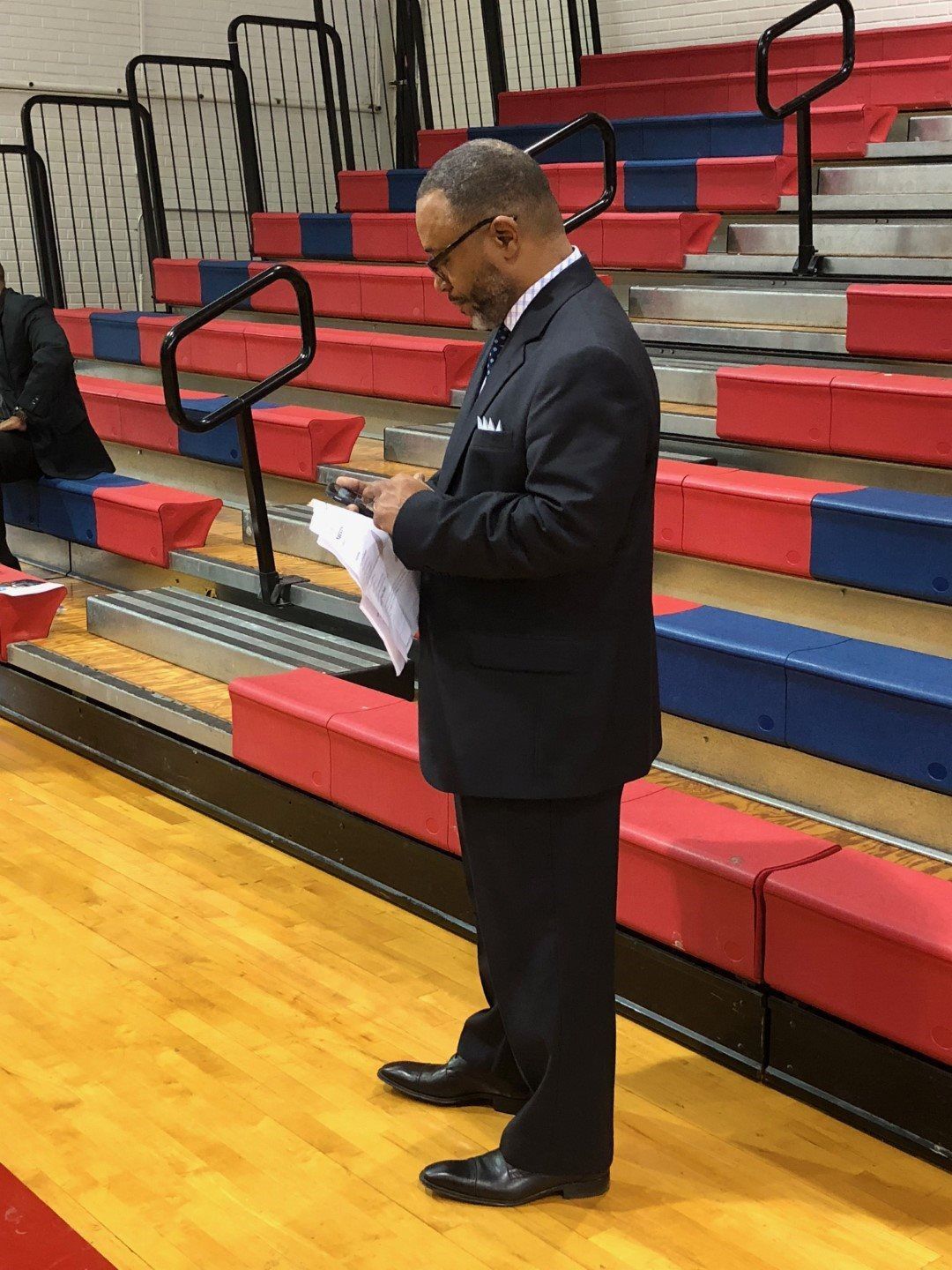 A man in a suit is standing in front of a bleacher.