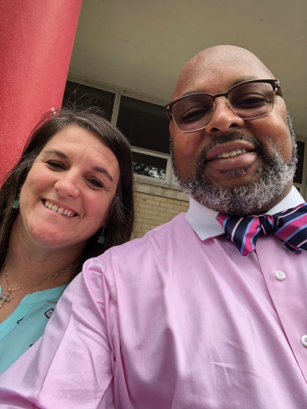 A man in a pink shirt and bow tie is taking a selfie with a woman.