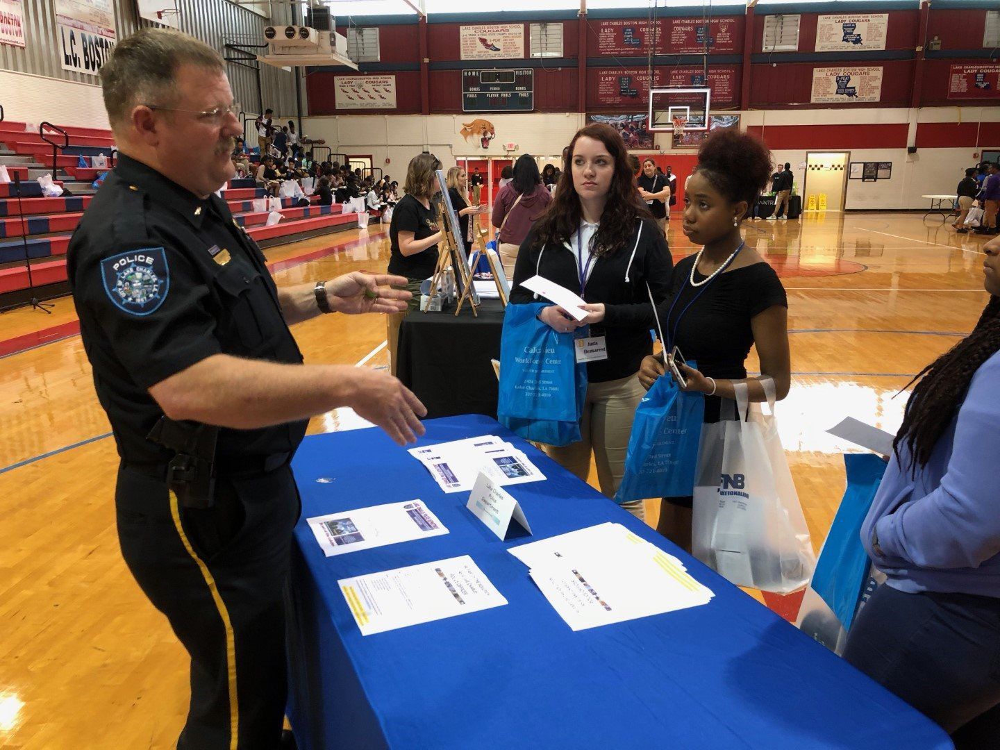 A police officer is talking to a group of people at a table in a gym.