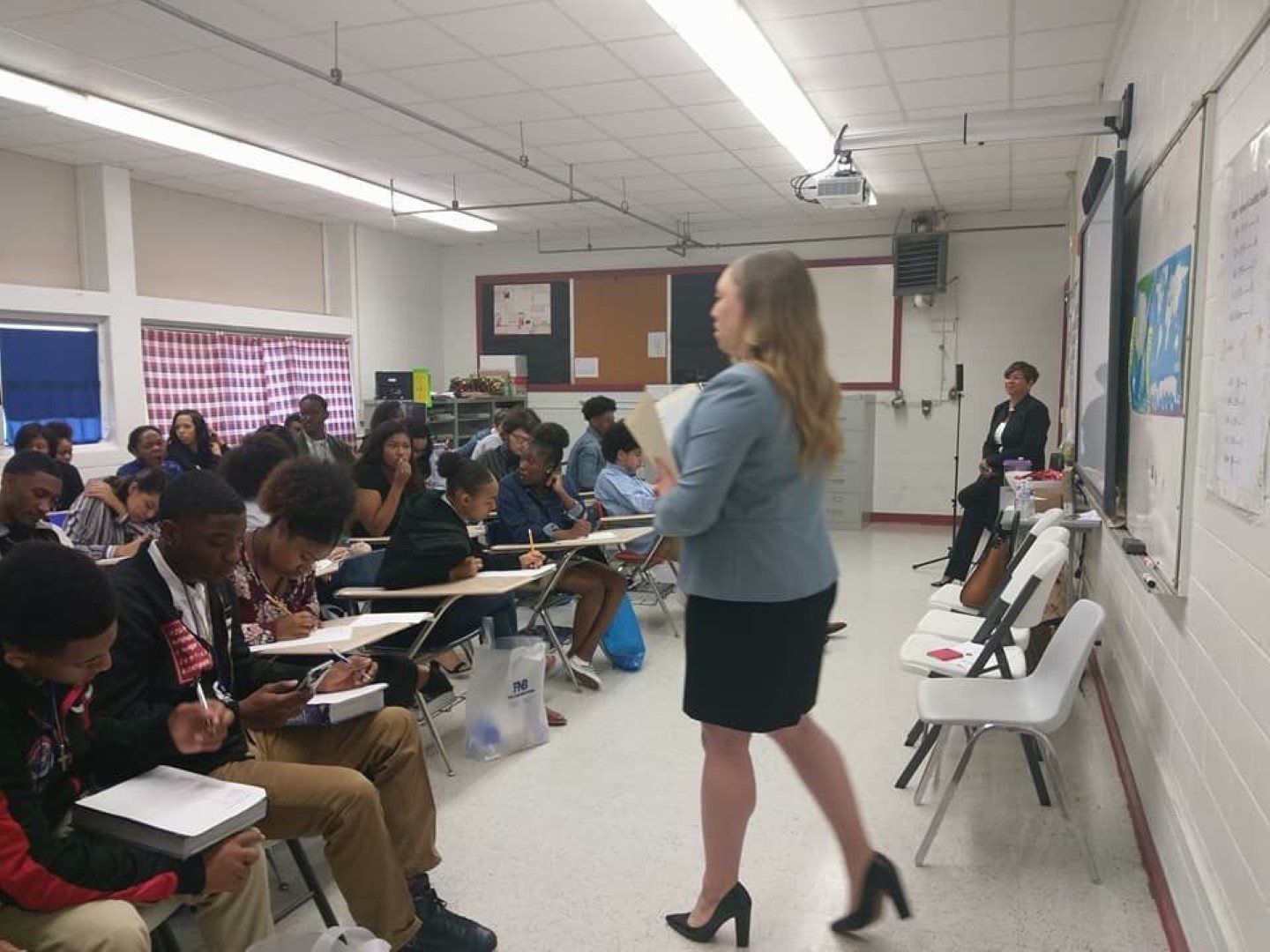 A woman is giving a presentation to a group of students in a classroom.