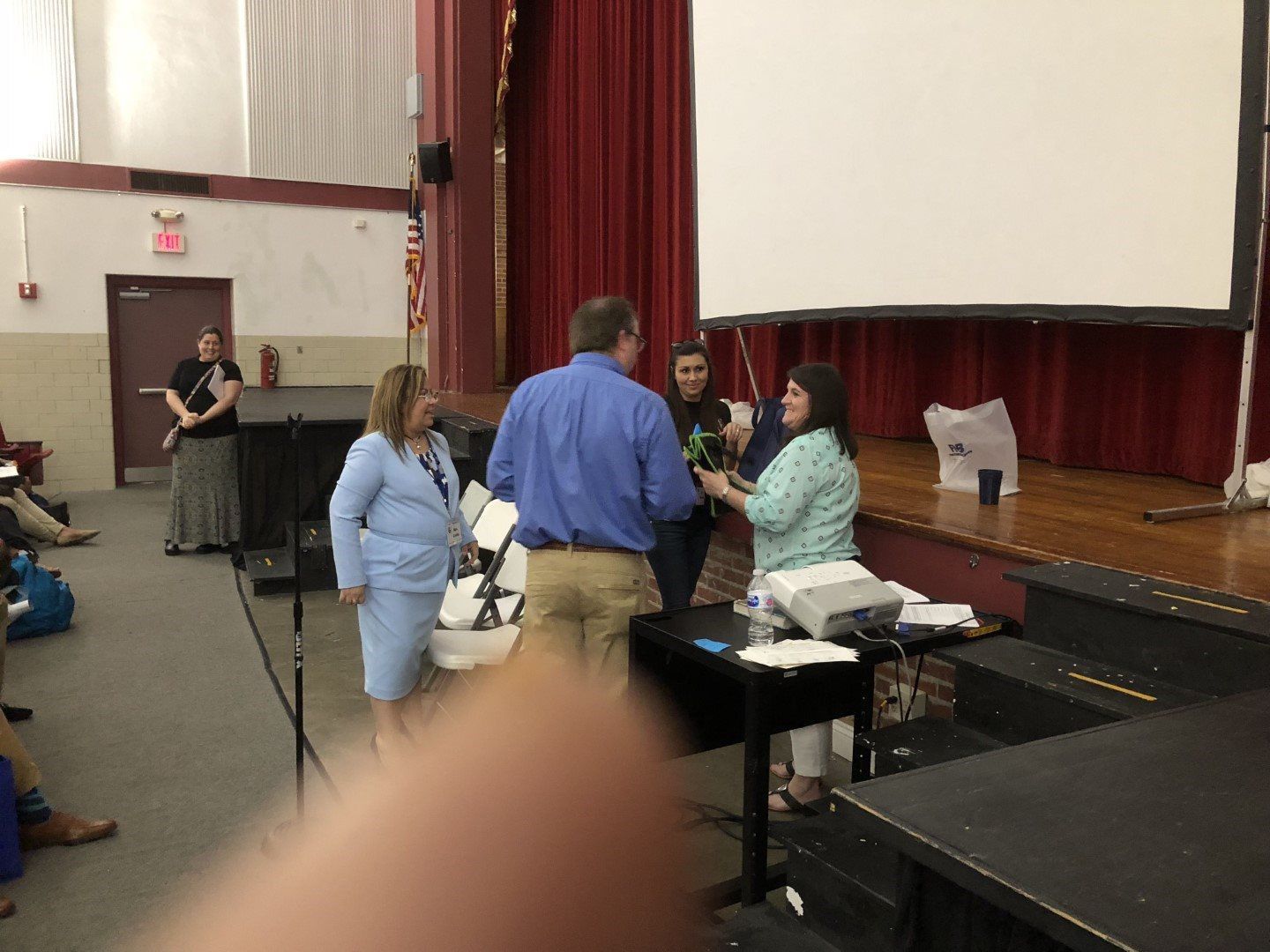 A group of people are standing on a stage in front of a projector screen.