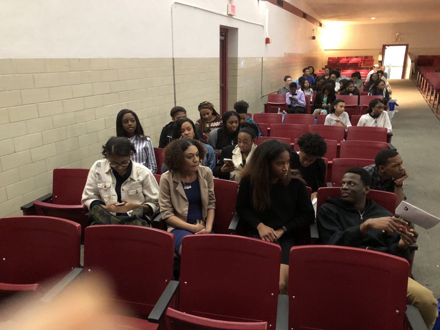 A group of people are sitting in red chairs in an auditorium.