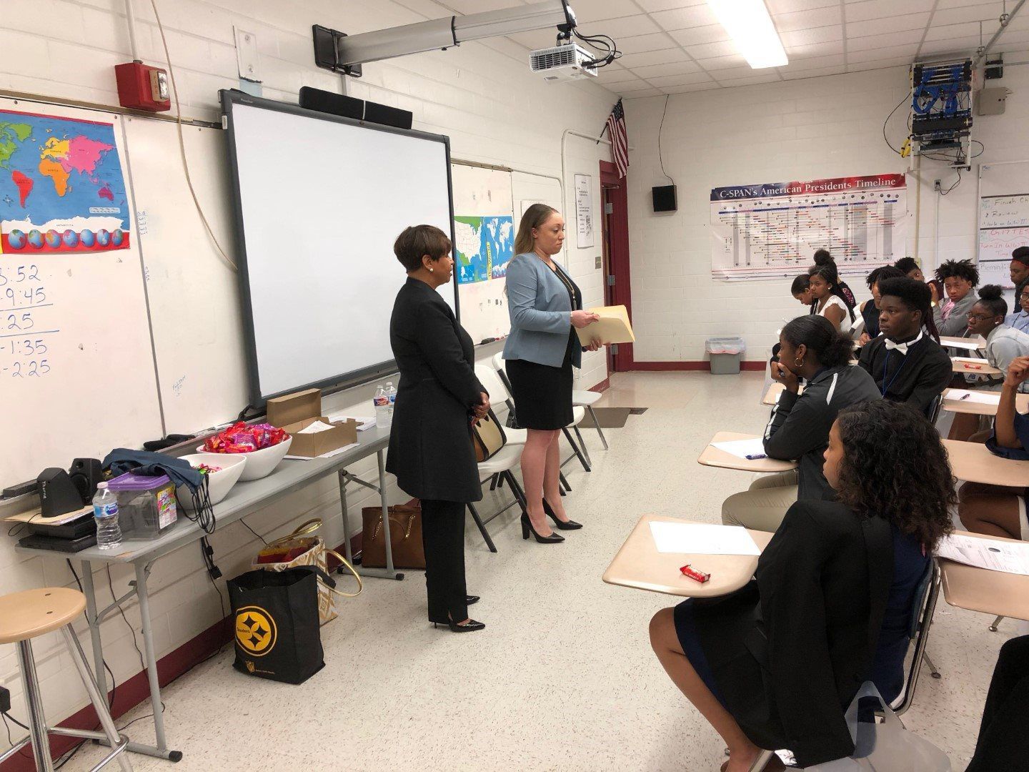 Two women are standing in front of a group of students in a classroom.