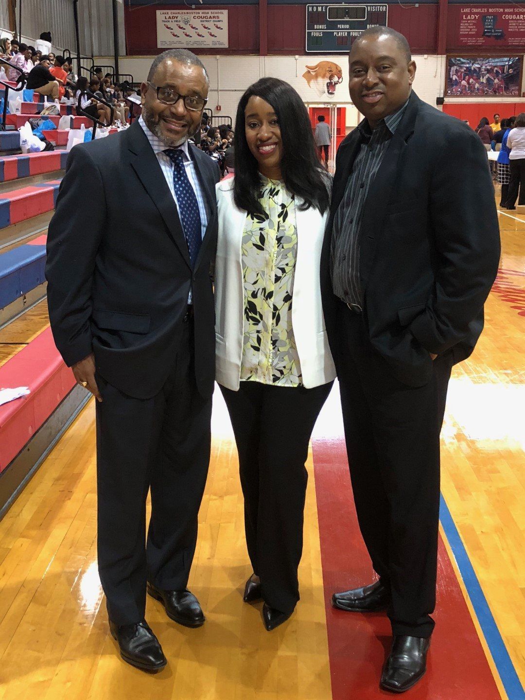 Three men and a woman are posing for a picture on a basketball court.