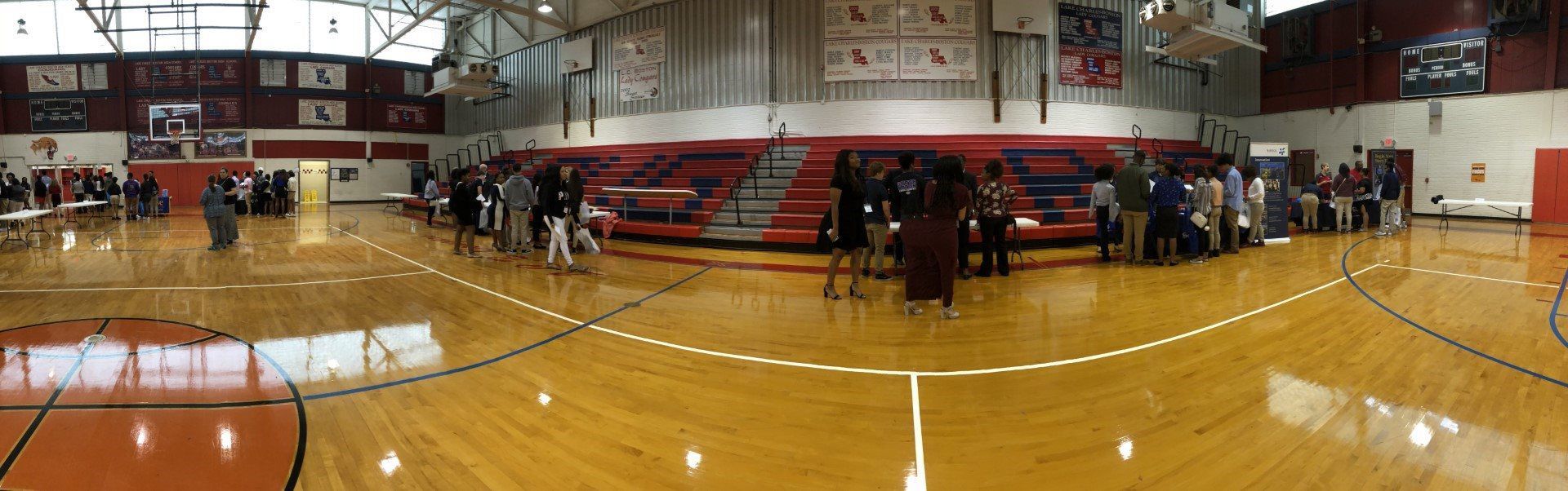 A group of people are standing around a basketball court in a gym.