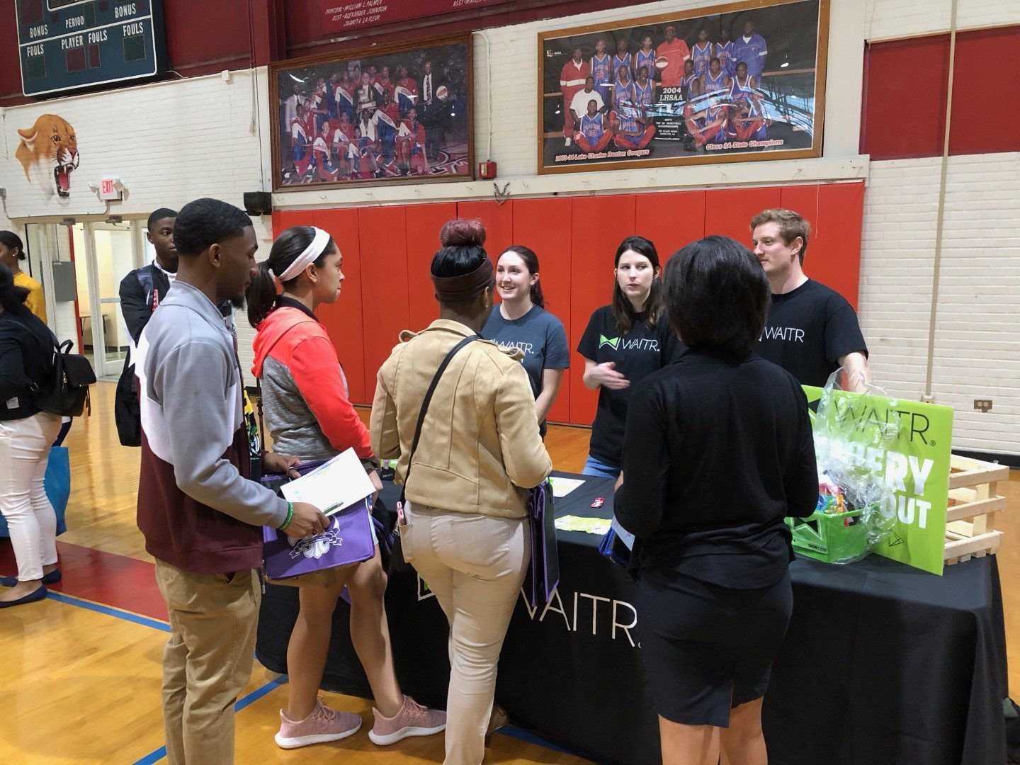 A group of people are standing around a table in a gym.