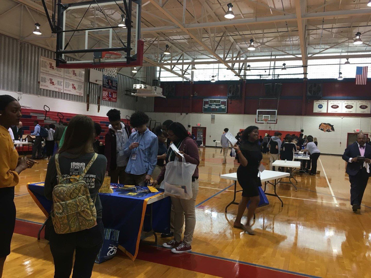 A group of people are standing around tables in a gym.