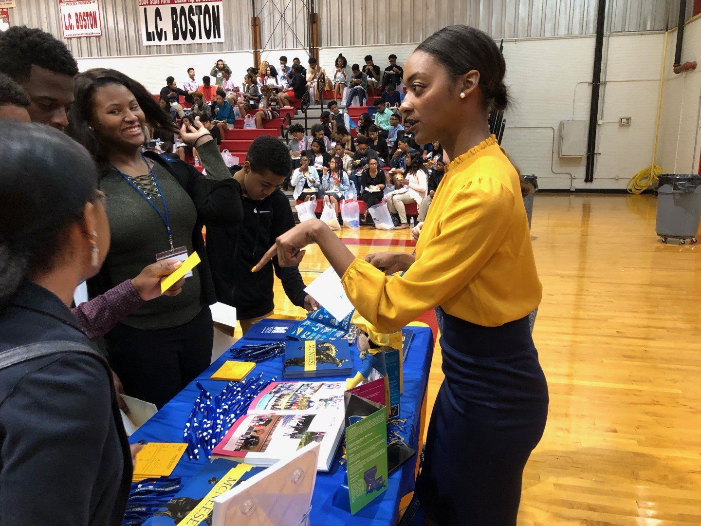 A woman is standing at a table talking to a group of people.