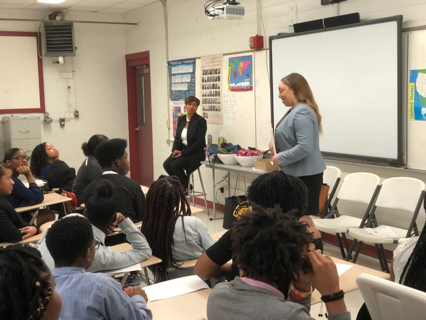 A woman is giving a presentation to a group of students in a classroom.