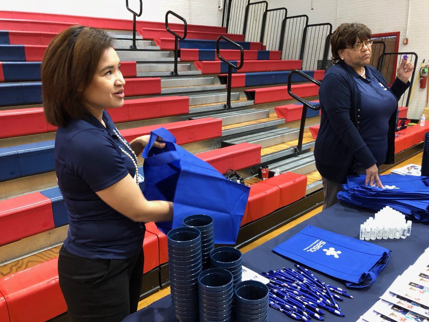Two women are standing in front of a table in a gym.
