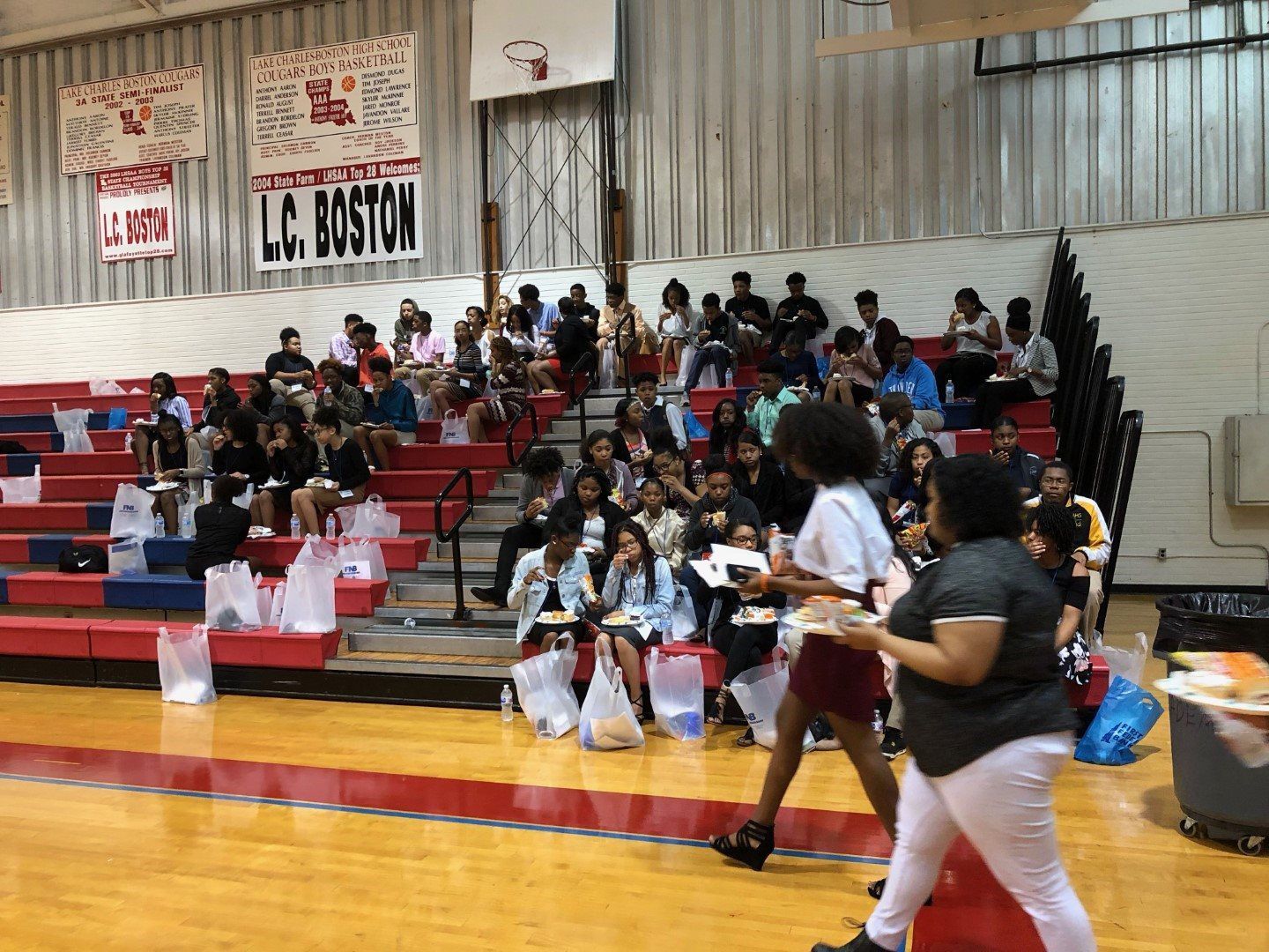 A group of people are standing on a basketball court in front of a sign that says lc boston.