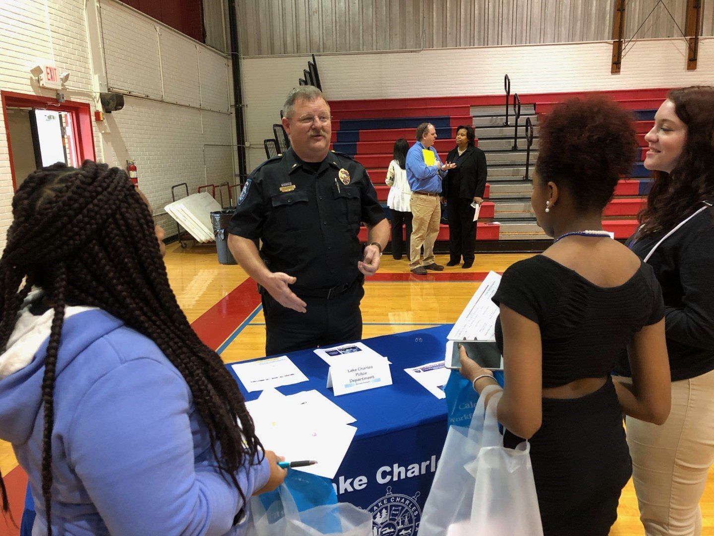 A police officer is talking to a group of people at a table in a gym.