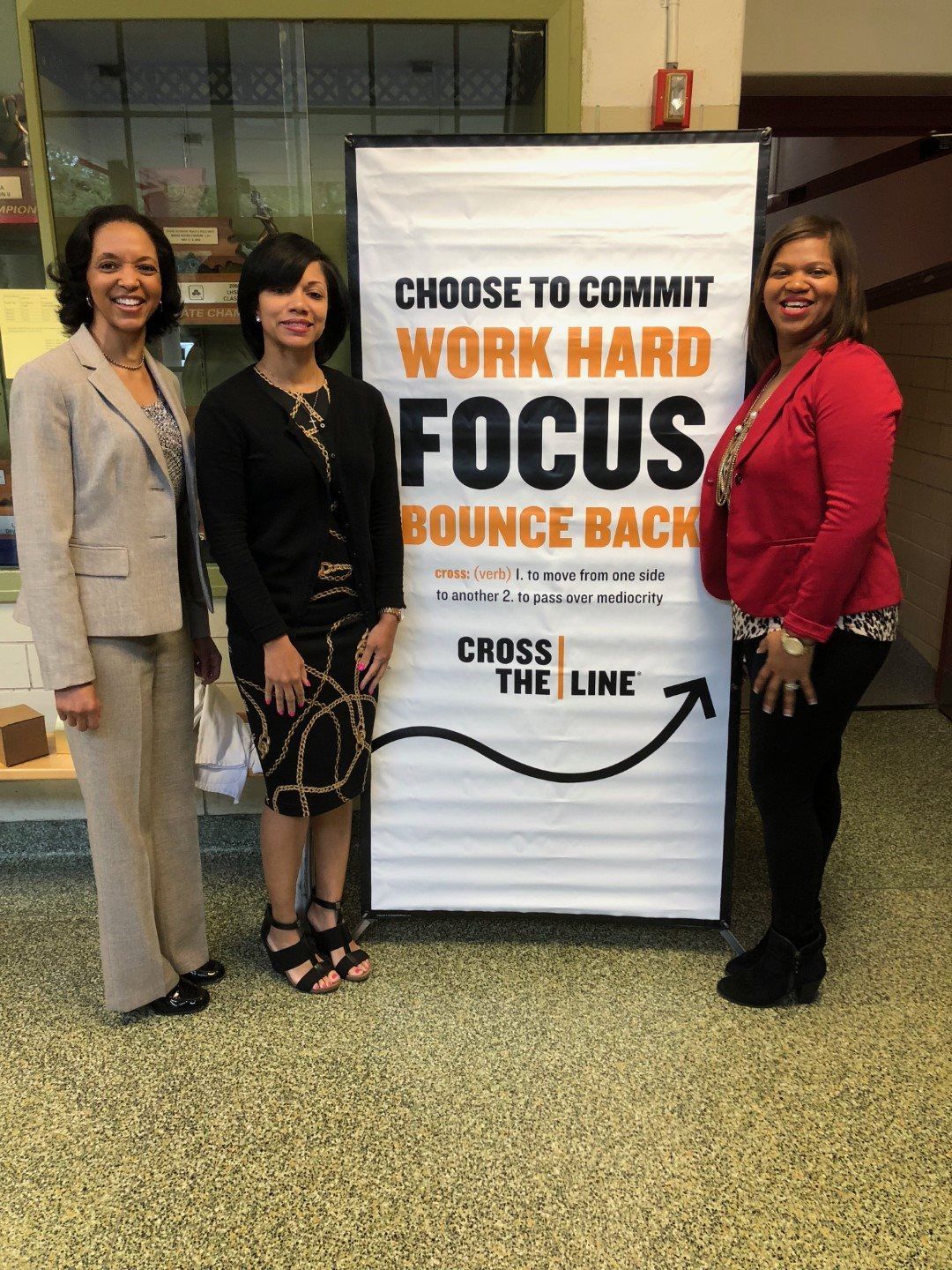 Three women are standing in front of a sign that says `` choose to commit work hard focus bounce back ''.