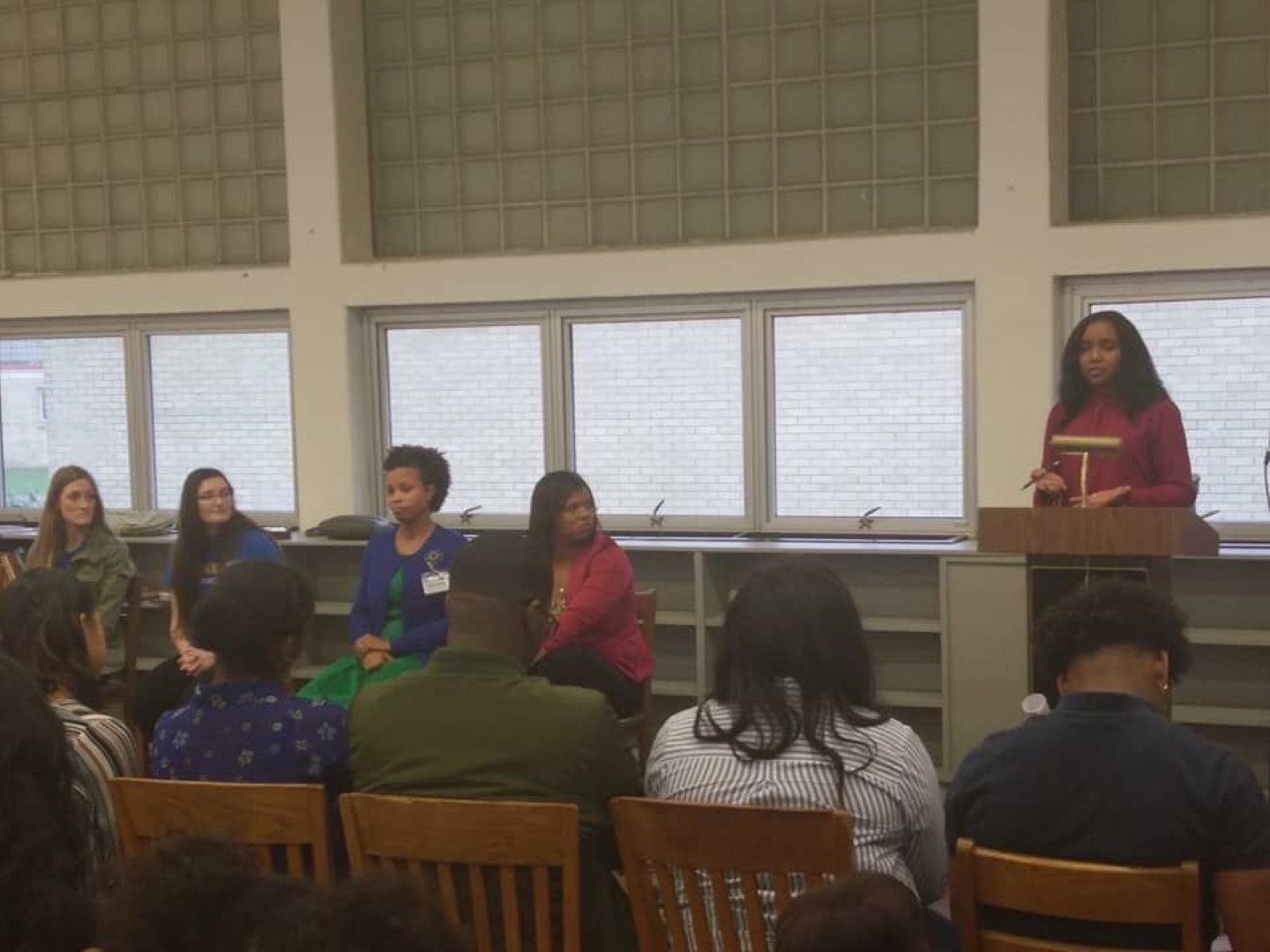 A woman is standing at a podium giving a speech to a group of people sitting in chairs.
