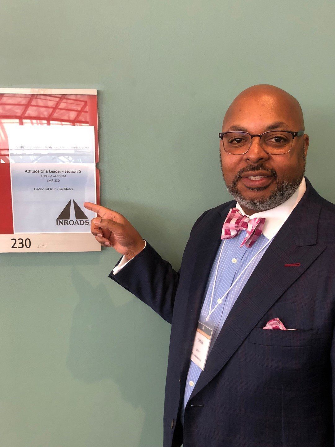 A man in a suit and tie is pointing at a sign on a wall.